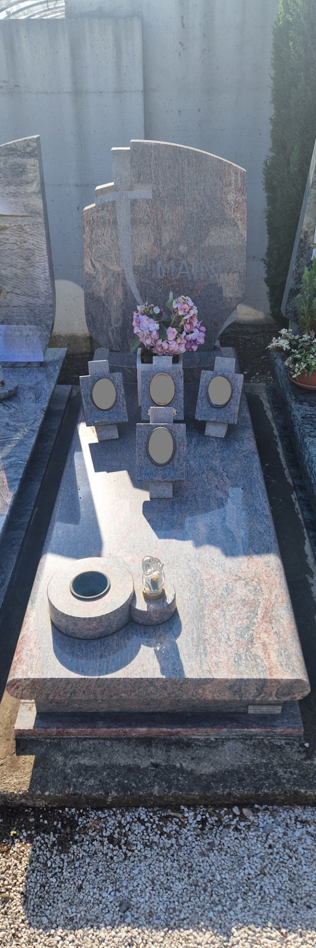 Tomba in granito venato blu e rosa con croce in rilievo e portaritratti in pietra