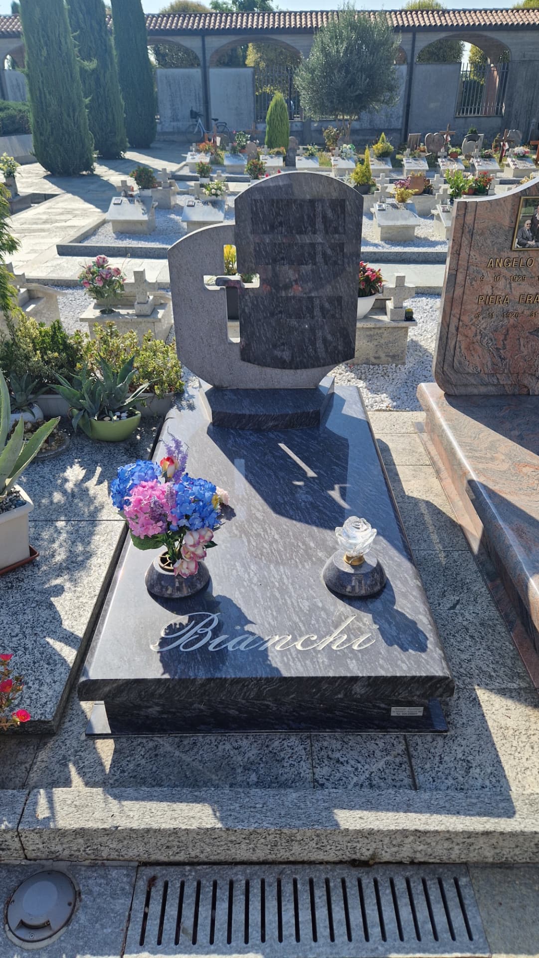 Tomba in granito scuro venato con stele arrotondata e incisione del cognome
