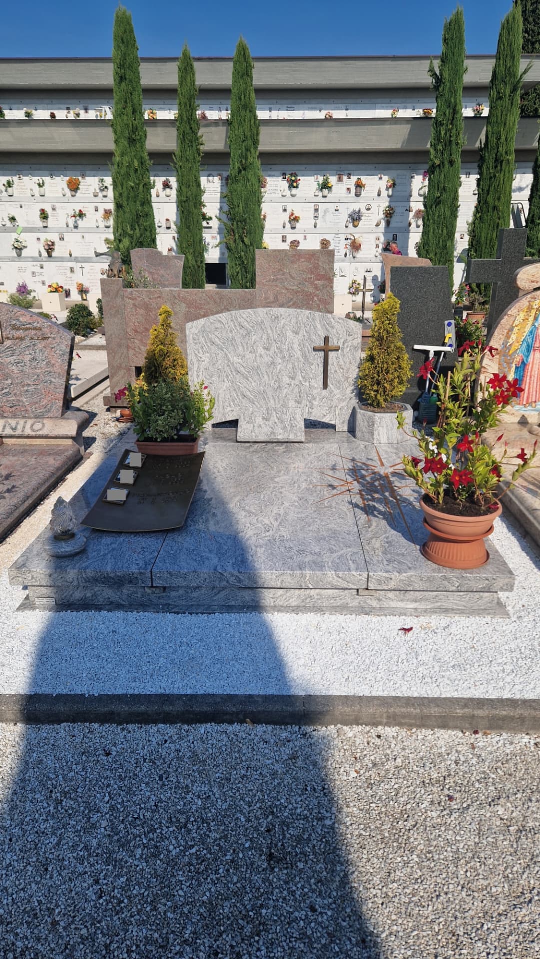 Tomba di famiglia in granito chiaro con stele ad arco e croce in bronzo