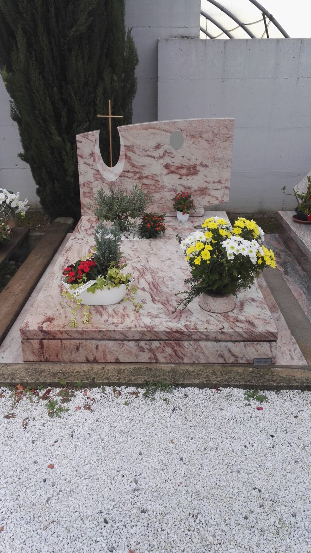 Tomba in marmo rosa venato con stele sagomata e croce in ottone