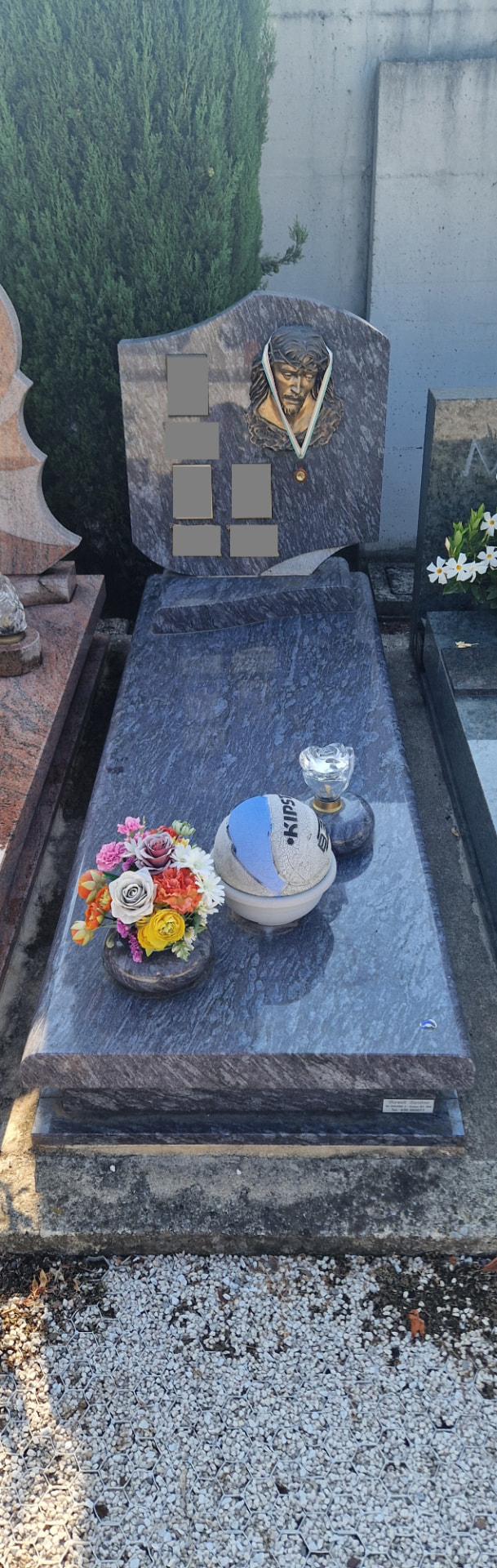 Tomba in granito venato blu con stele sagomata e volto di Cristo in bronzo