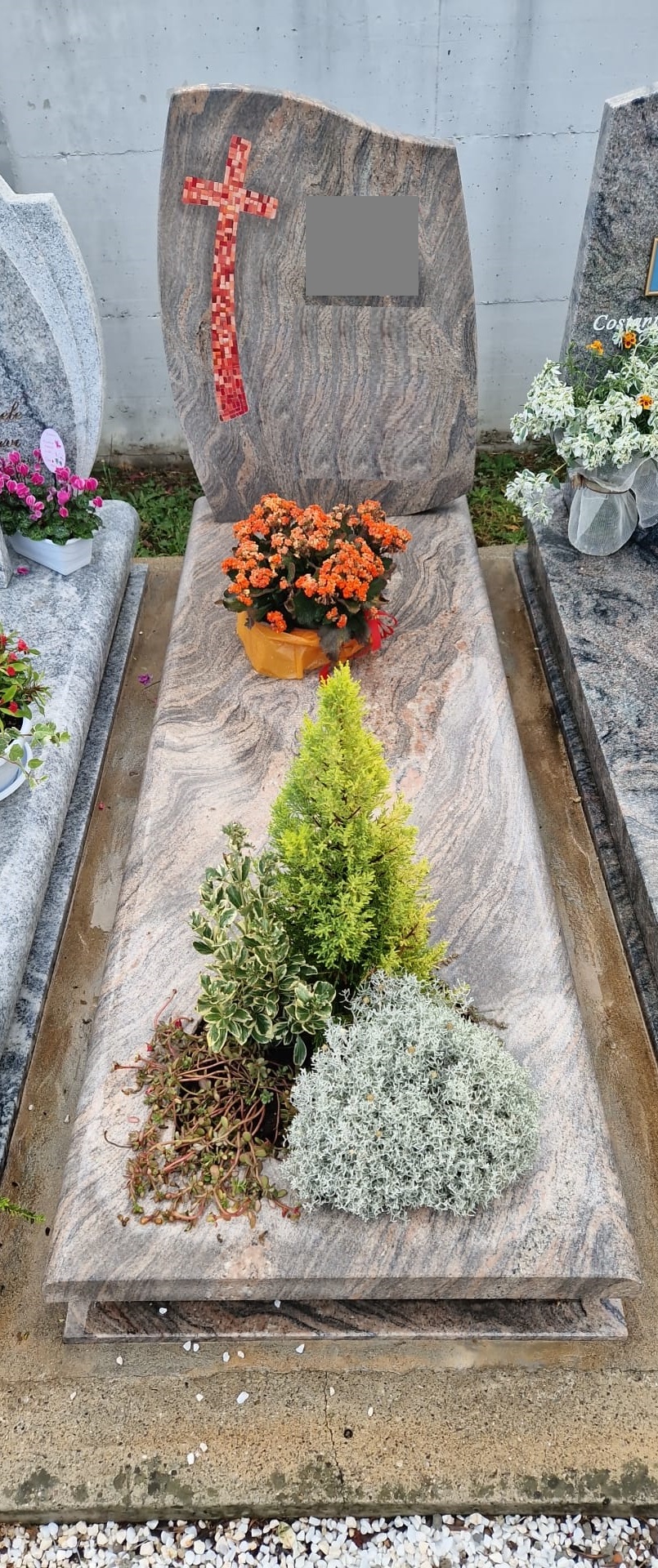 Tomba in granito rosato con croce in mosaico rosso e aiuola di piante