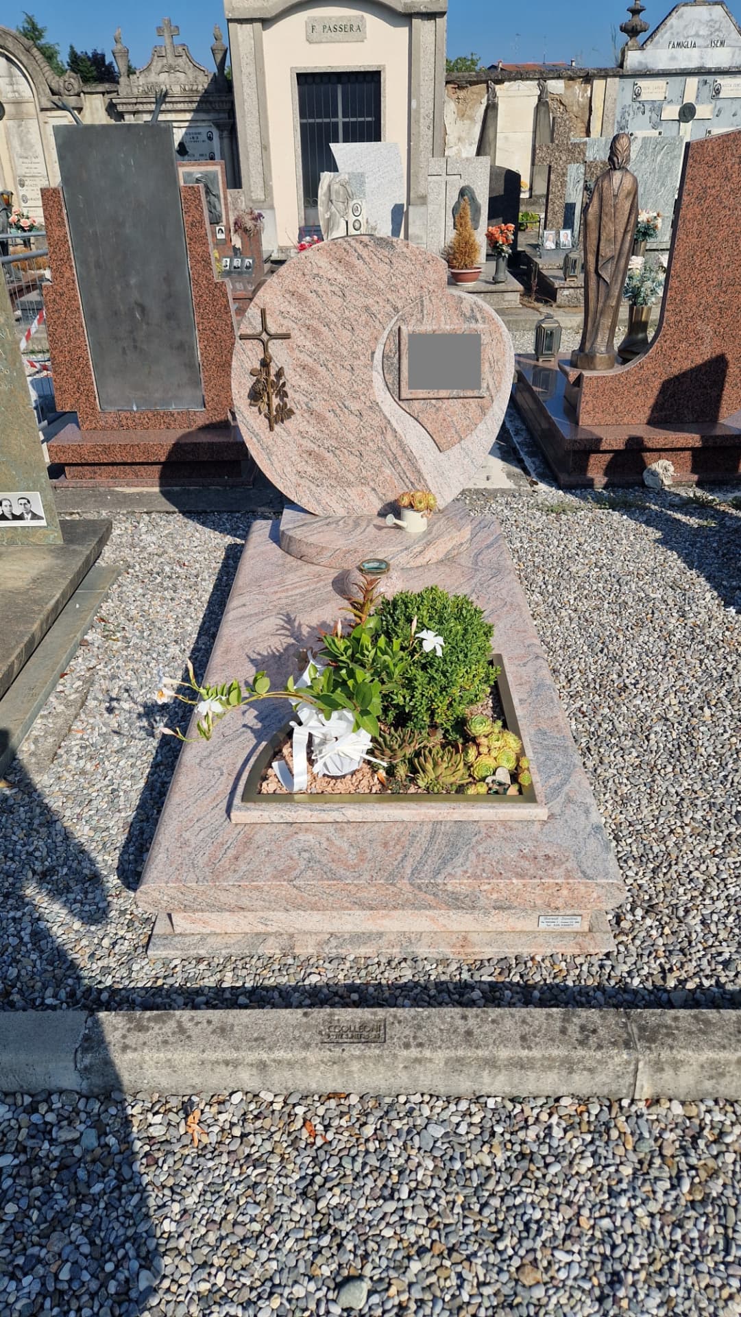 Tomba in granito rosa con stele tonda, croce bronzea e giardino di piante grasse