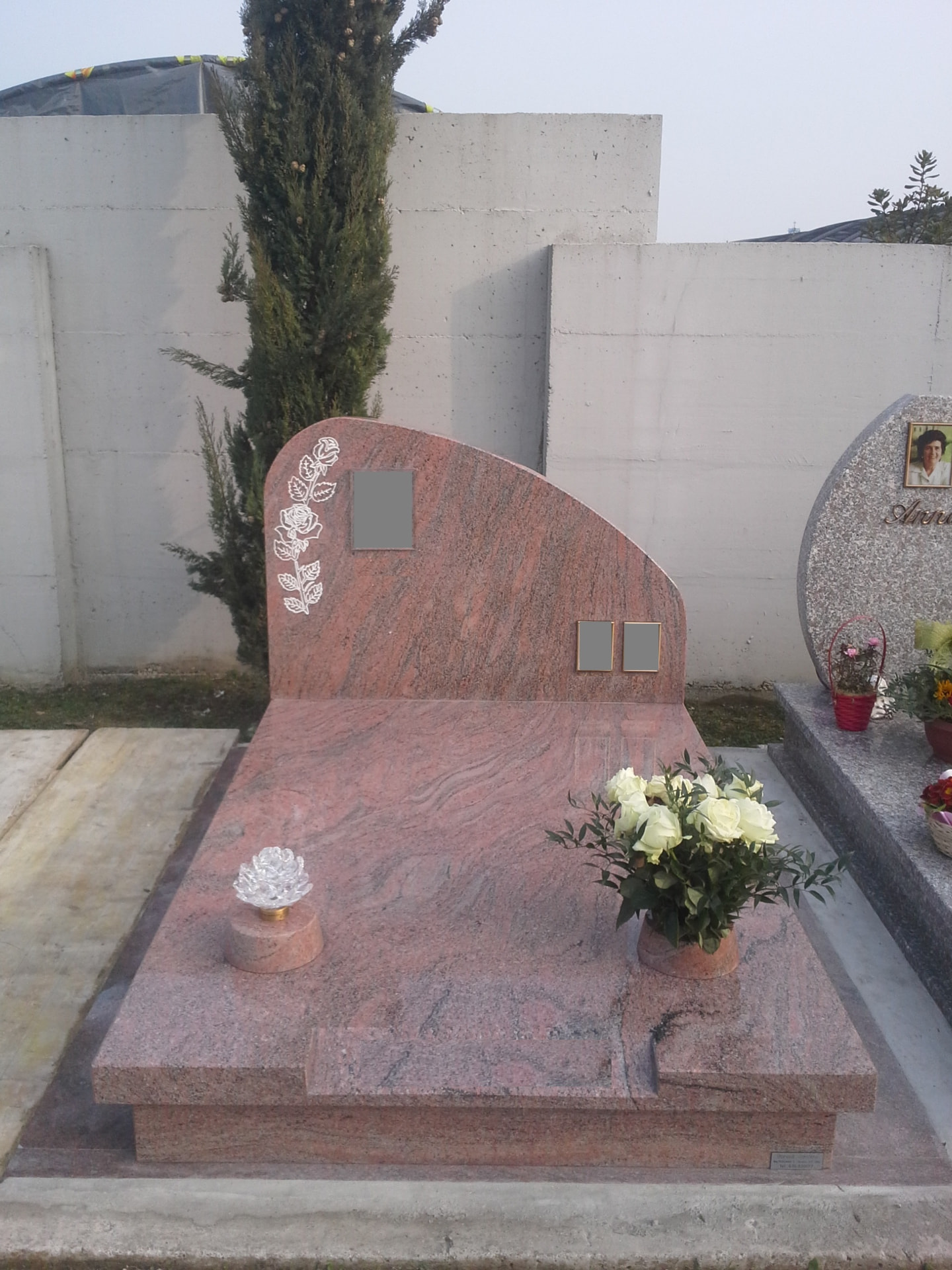 Tomba in granito rosso venato con stele curva e incisione di rose