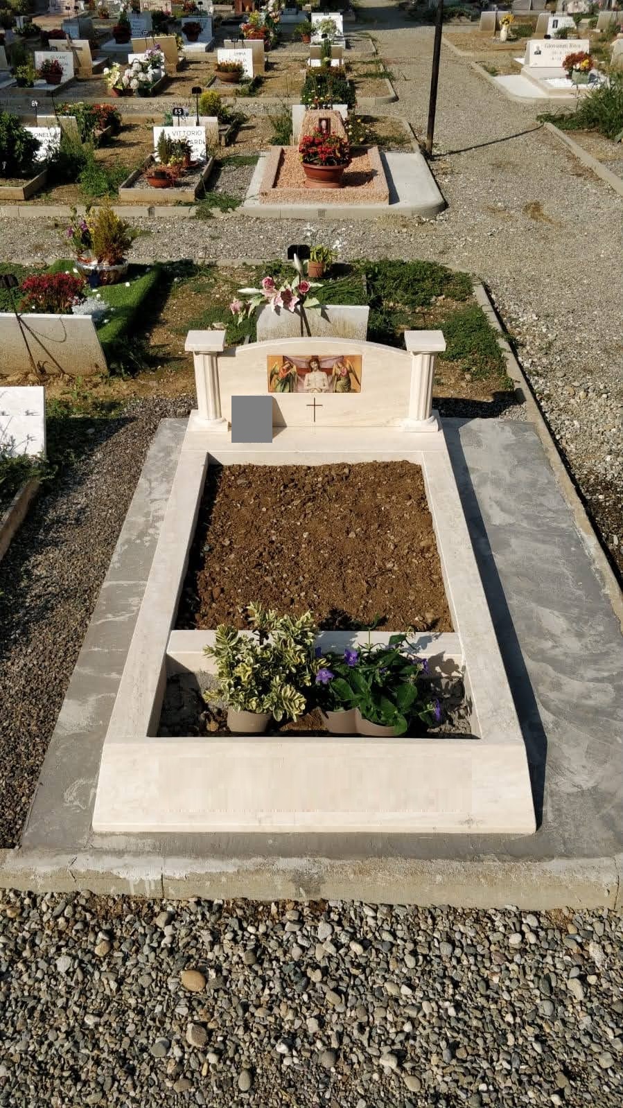Tomba in pietra chiara con stele a colonnine, mosaico sacro e aiuola in terra