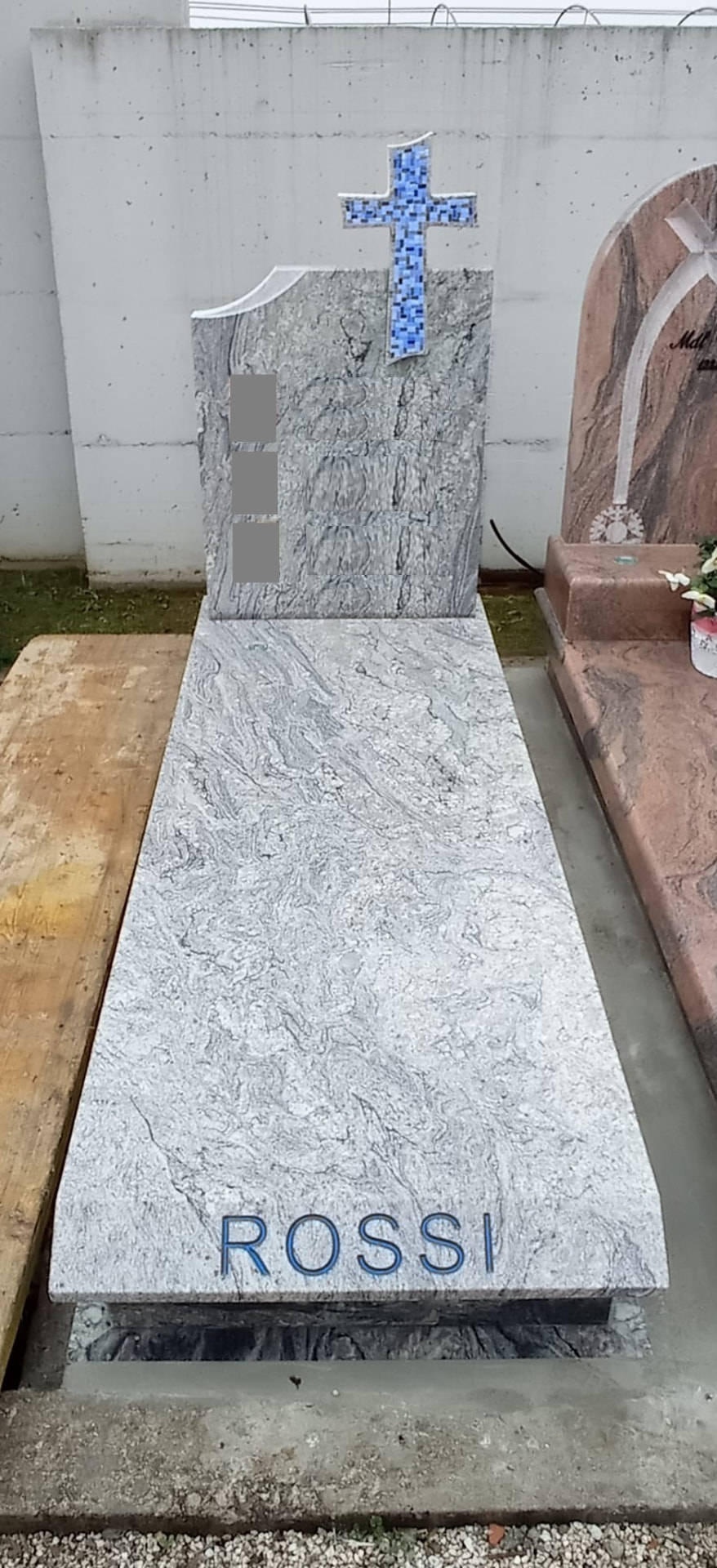 Tomba in granito bianco venato con croce in mosaico azzurro e incisione del cognome