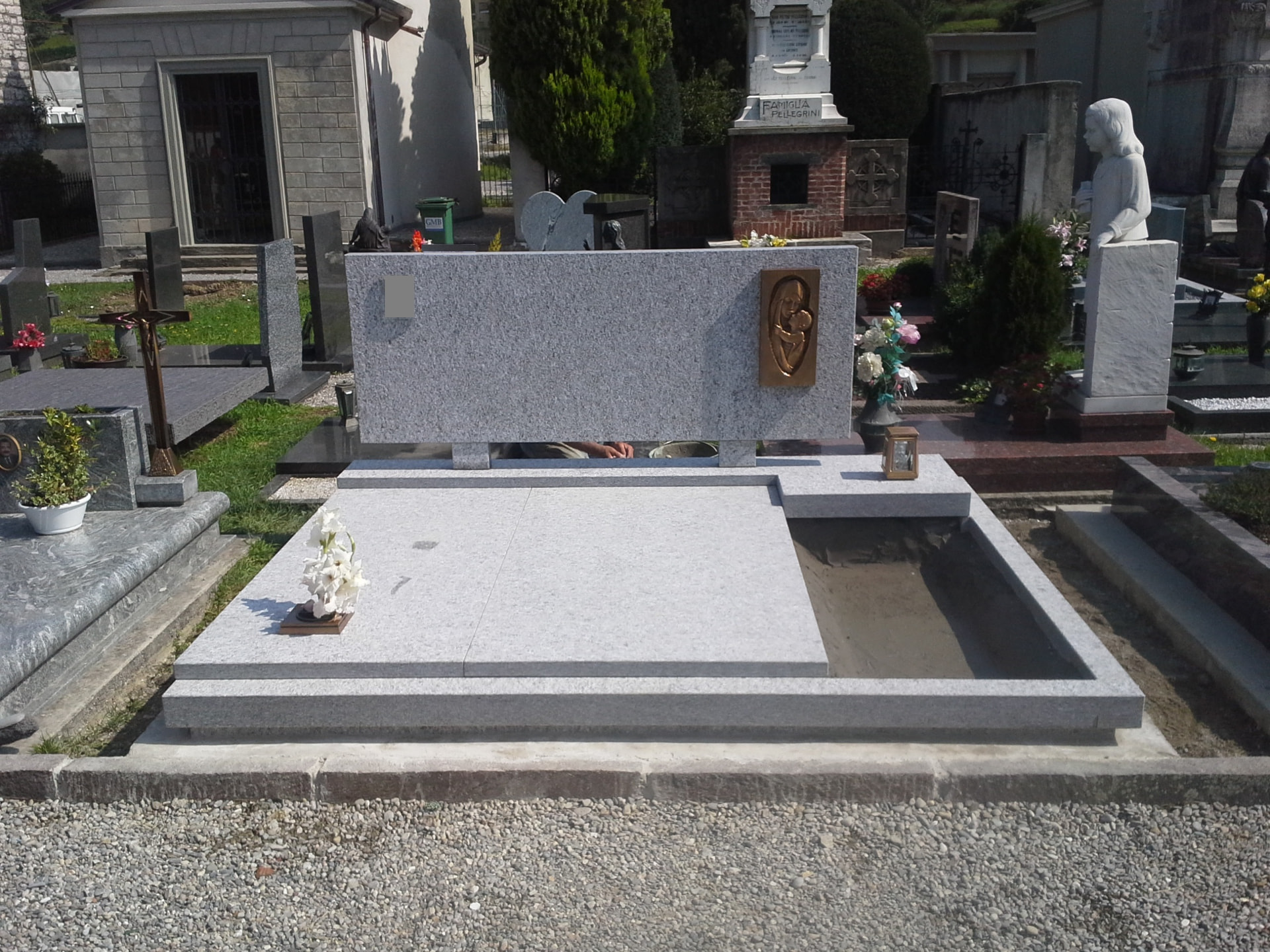 Tomba in granito bianco con stele lineare e formella bronzea della Madonna con Bambino