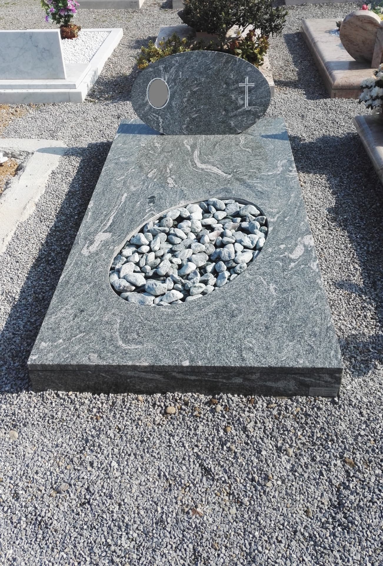 Tomba in granito verde venato con stele ovale, croce incisa e ovale in ciottoli