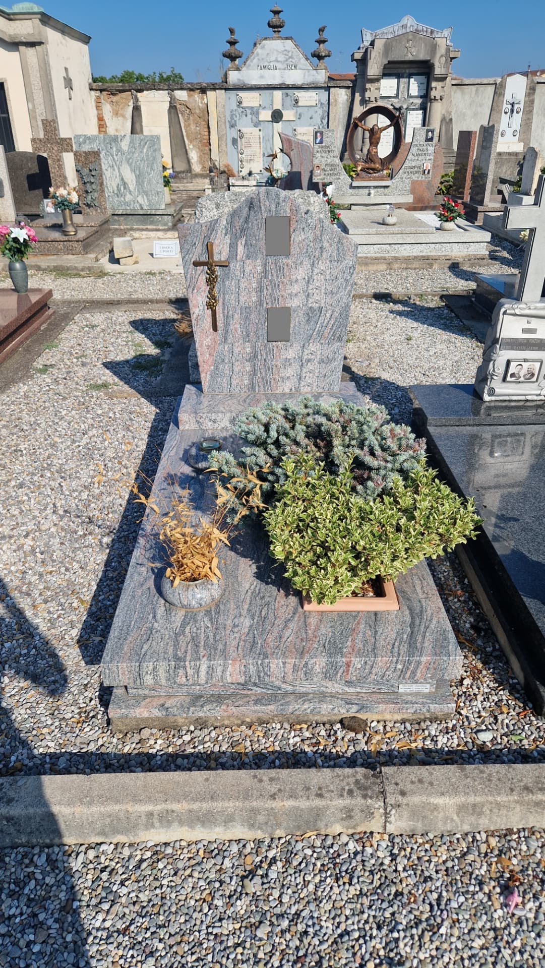 Tomba in granito multicolor con croce bronzea e aiuola verde