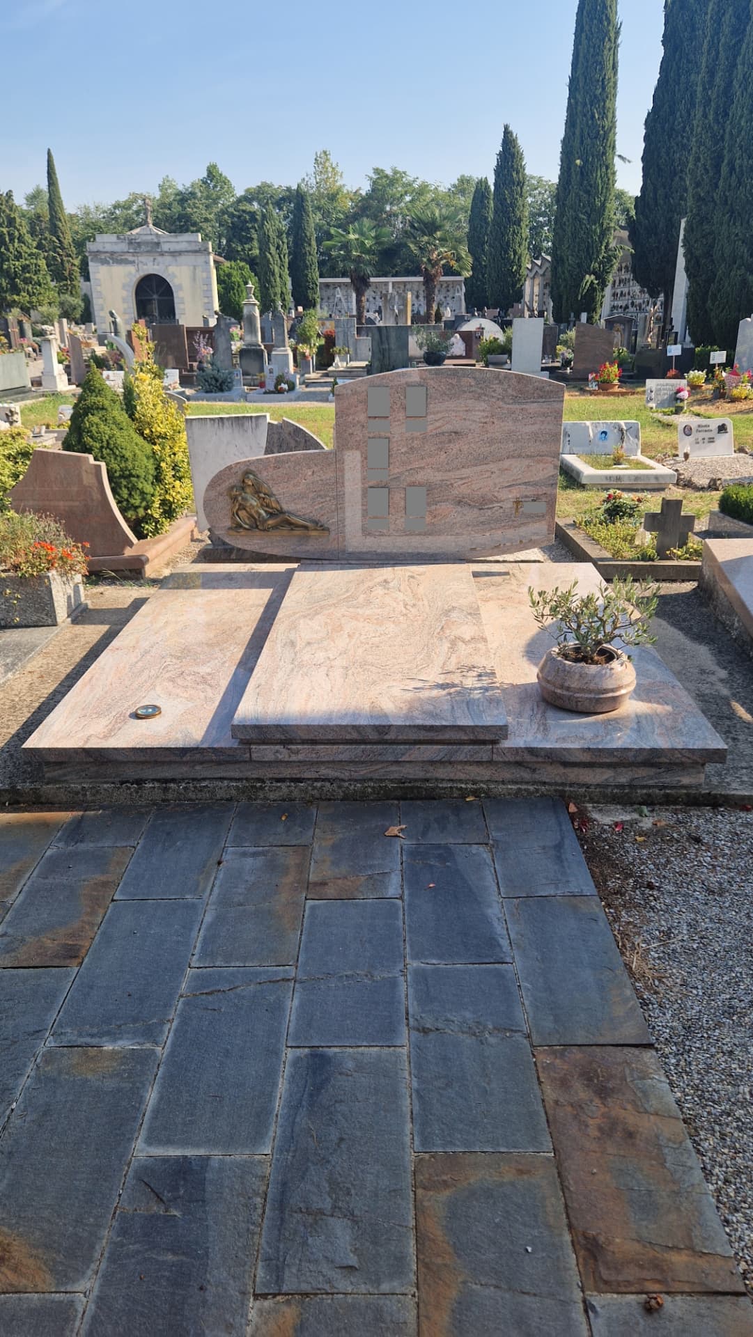 Tomba di famiglia in granito rosa con stele curva e bassorilievo bronzeo della Pietà