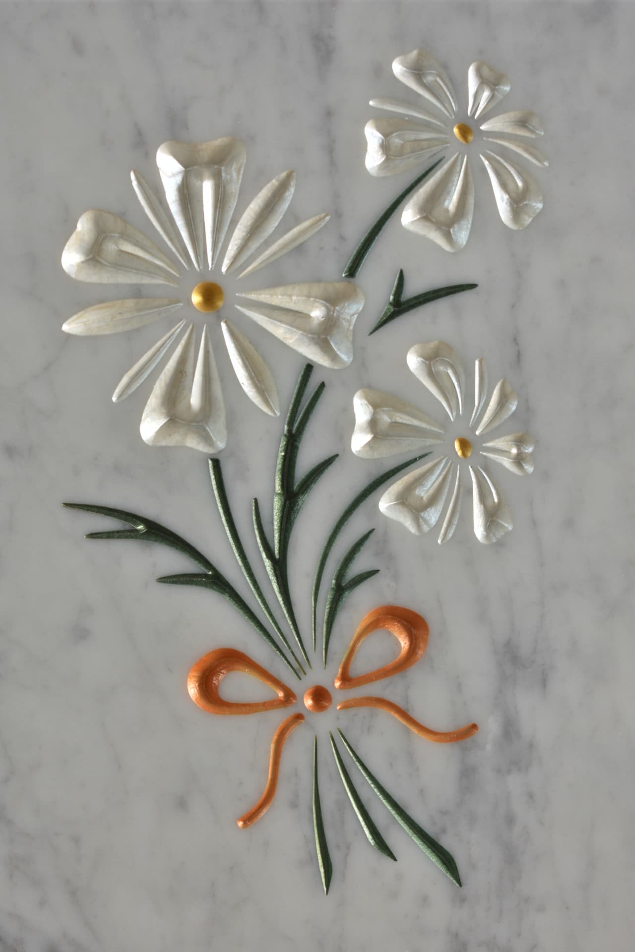 Fiori bianchi e fiocco arancione incisi su marmo