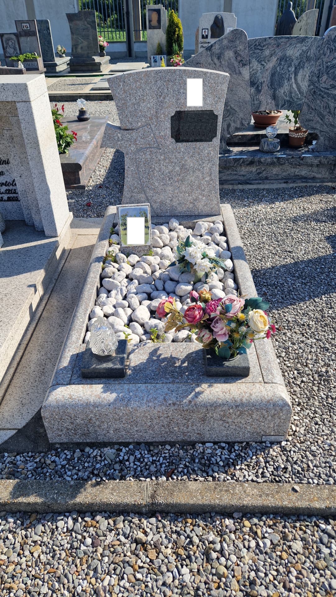 Tomba in granito rosa con stele a croce e giardino di ciottoli bianchi