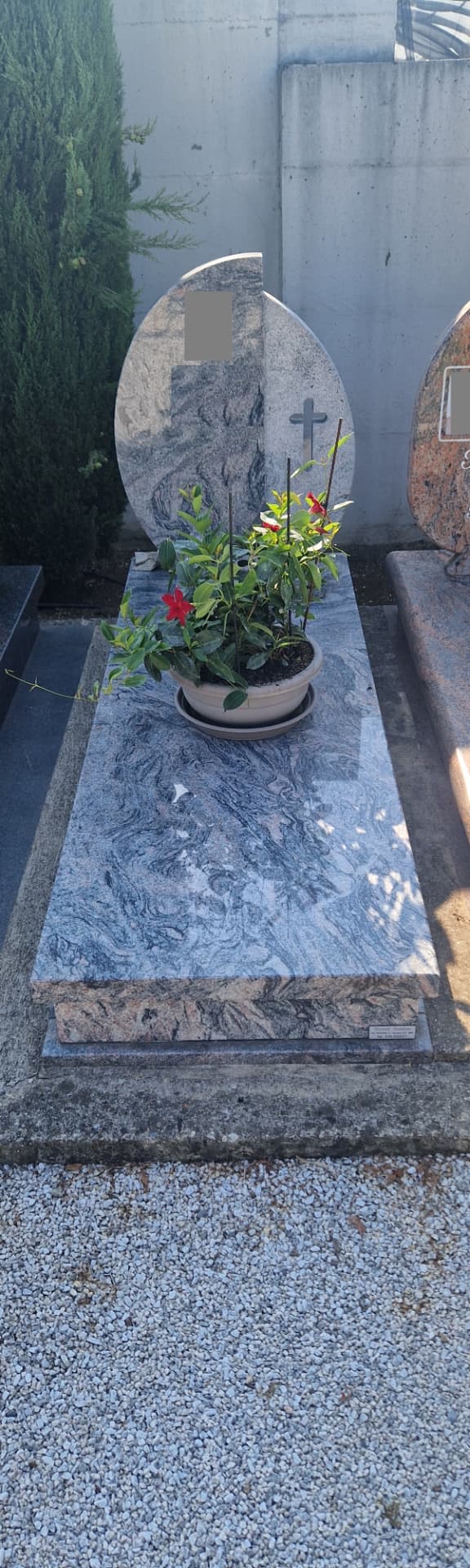 Tomba in granito grigio venato con stele ovale, croce incisa e aiuola fiorita