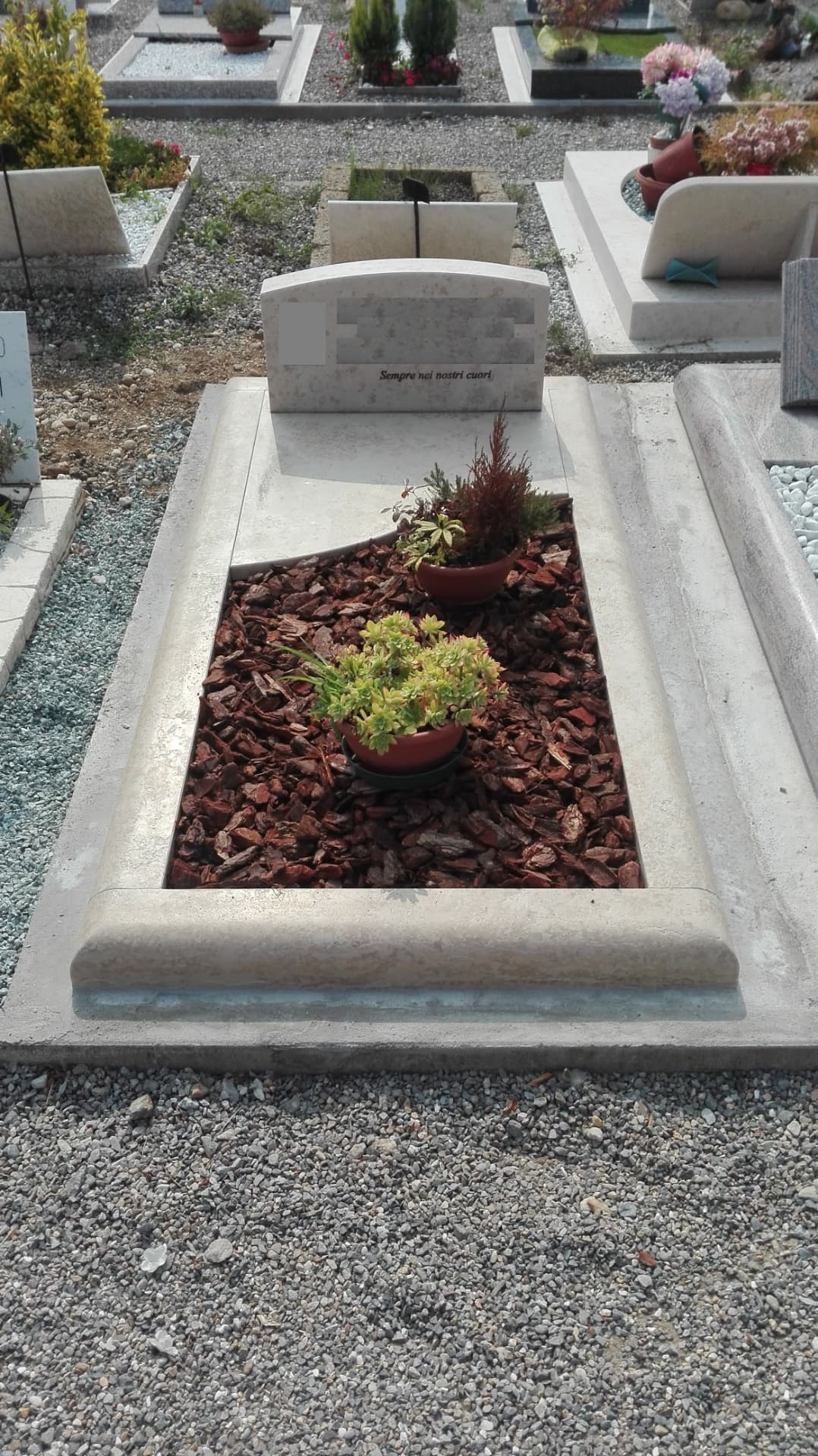 Tomba in pietra chiara con cornice modanata, stele ad arco e aiuola in corteccia