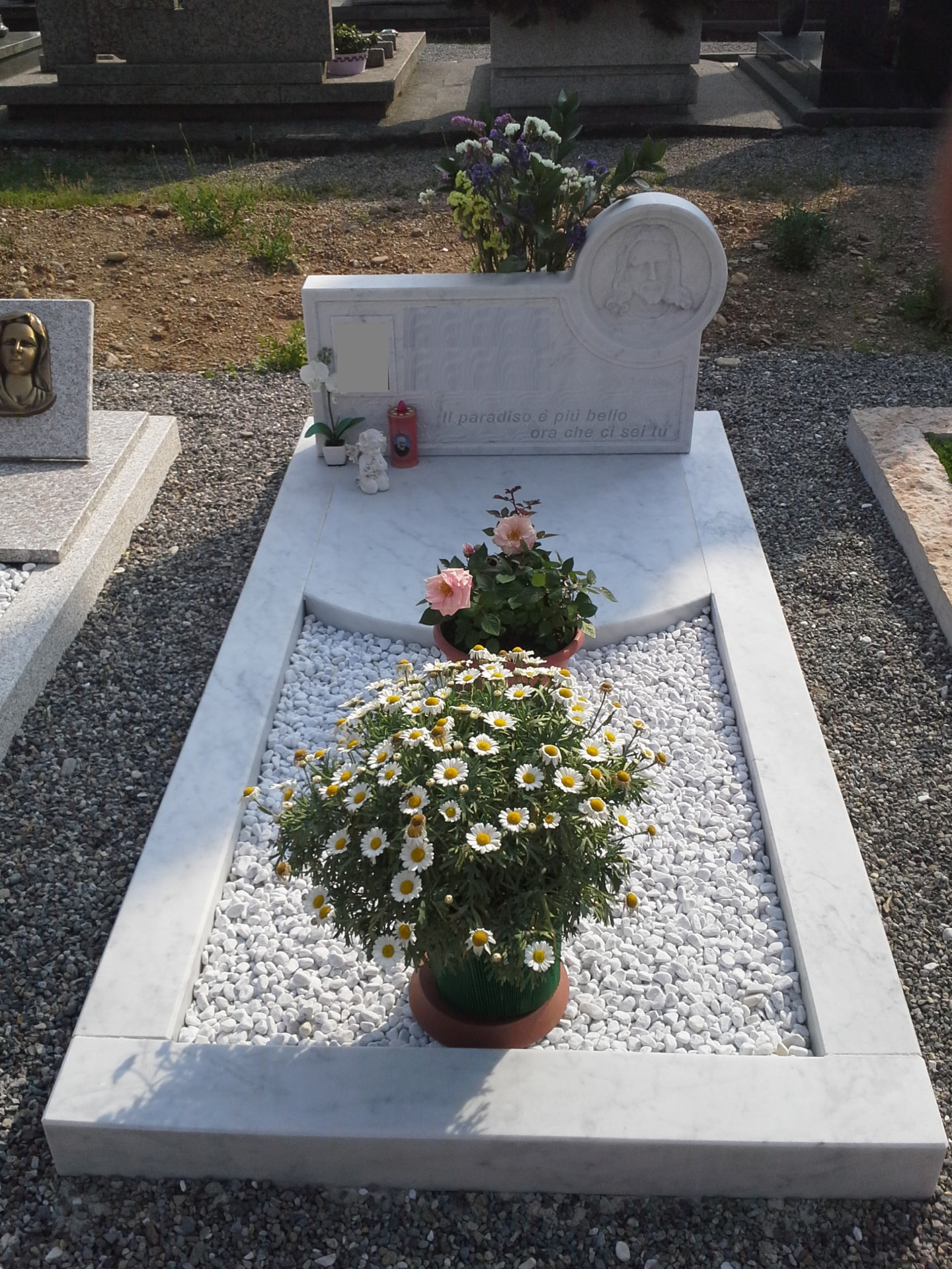Tomba in marmo bianco con stele scolpita del volto di Cristo e aiuola in ghiaia bianca