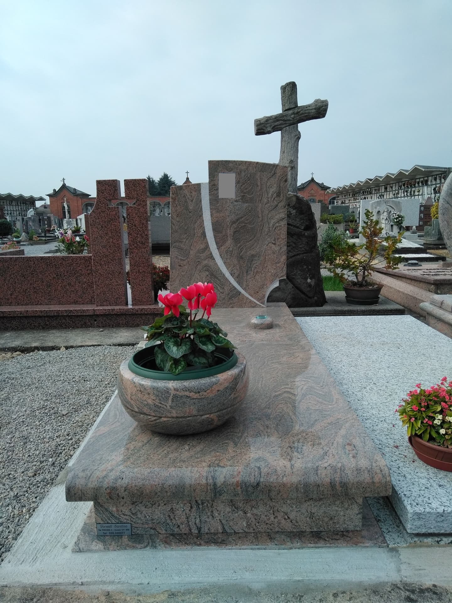 Tomba in granito rosato con stele curva e croce in pietra